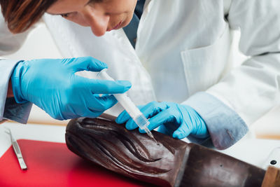 Restoring wooden craft statue. restores hands in protective gloves filling cracks using syringe