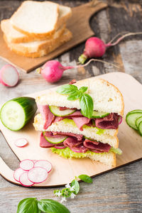 Double sandwich with pastrami and fresh vegetables and herbs on a cutting board. american snack