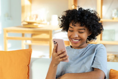 Young woman using mobile phone while sitting on bed at home