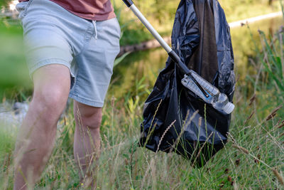 Man volunteer picking up a discarded plastic bottle into a black trash bag from grass.