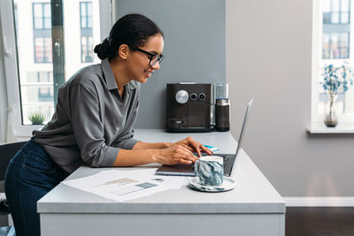 Side view of smiling woman using laptop on table at home