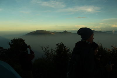 Rear view of silhouette friends against mountains during sunset