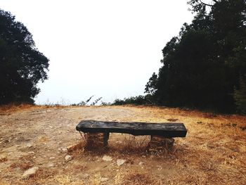 Empty bench on field against clear sky