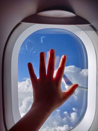 Cropped image of hand on window against sky