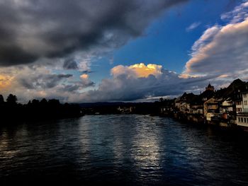 Scenic view of river by buildings against sky during sunset