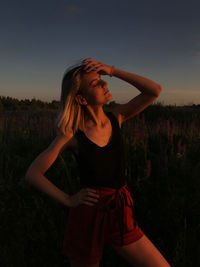 Young woman standing by plants against sky during sunset