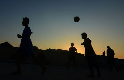 Silhouette people playing with ball on beach against sky during sunset