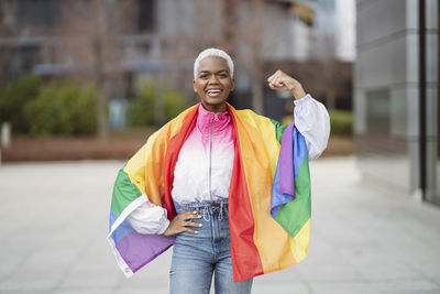 Young woman wrapped in rainbow flag flexing muscle with hand on hip