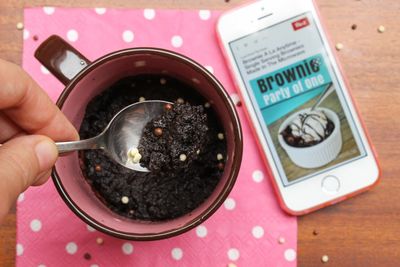 Cropped hand holding spoon with brownie over cup at table