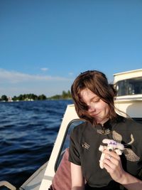 Young woman holding stuffed toy while standing in boat on sea against blue sky during sunny day