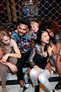Trendy multiracial young friends smiling together while sitting on concrete steps at night party