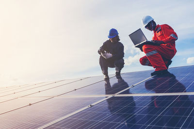 Low angle view of male technicians working on solar panels against sky