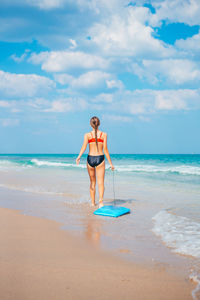 Rear view of woman standing at beach against sky