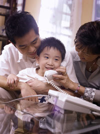 Smiling boy talking on landline phone while sitting with grandmother and father at home