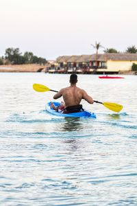 Rear view of shirtless man in kayaking in lake