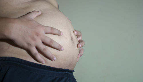 Midsection of shirtless overweight man with hands on stomach