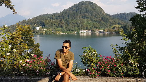 Man sitting on retaining wall by lake against mountains