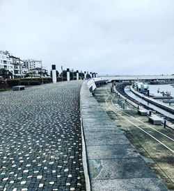 Footpath by railing in city against sky