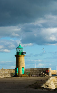 Lighthouse on road by building against sky