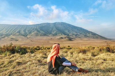 Low section of woman sitting on landscape against sky