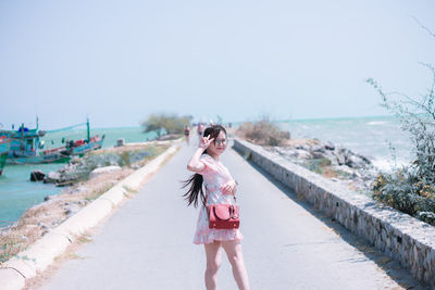 Portrait of woman wearing eyeglasses standing on footpath against sea and sky