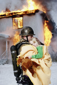 Fireman holding rescued girl, burning building in background