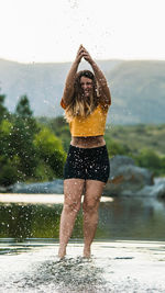 Full length portrait of woman splashing water while standing in lake