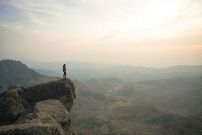 Man standing against mountains on cliff during sunset