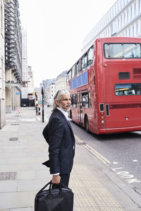 Uk, london, senior businessman with luggage waiting at crosswalk