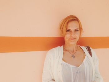 Portrait of a smiling young woman standing against wall