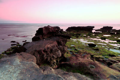 Rocks on shore against sky during sunset