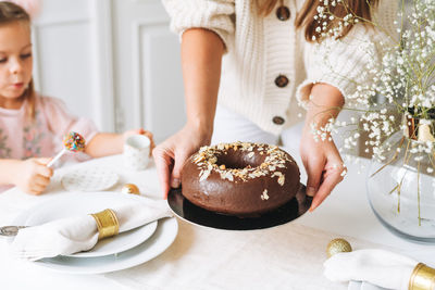 Young woman holding in hands large round chocolate almond cake on table with new year serving