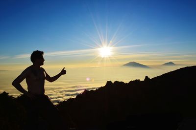 Silhouette man showing thumbs up on mountain peak against sky at sunset