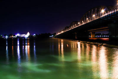 Illuminated bridge over river against sky at night