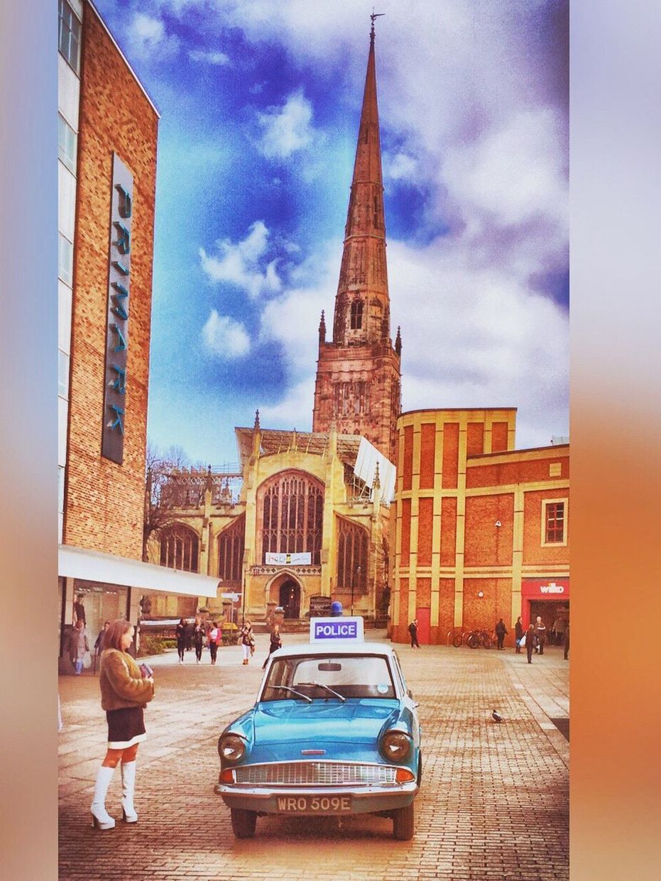 Woman standing by police car in front of church on street against sky in city