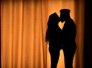 Silhouette couple kissing by curtain