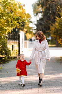 Happy mom and child are walking and having fun playing with autumn leaves in the fall park outdoors