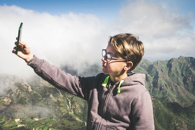 Man photographing with mobile phone against sky