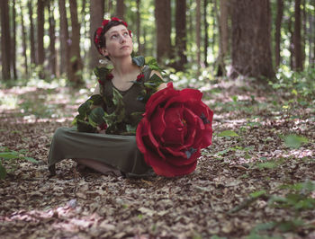 Beautiful young woman sitting on land in forest, staring at the trees