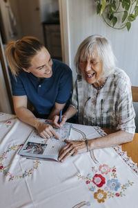 Happy senior woman solving puzzle while sitting with female care assistant at home