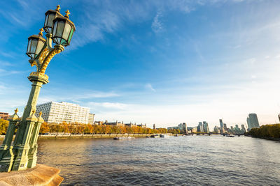 Street light by river and buildings against sky