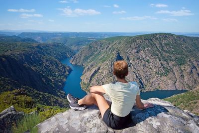 Rear view of woman sitting on mountain against sky