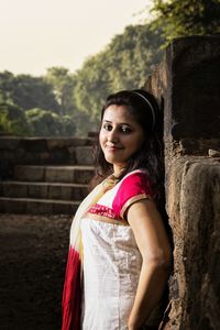 Portrait of smiling young woman standing against trees