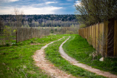 Dirt road amidst field against sky