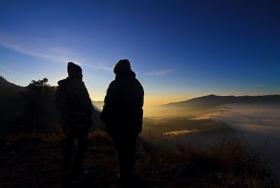 Rear view of silhouette couple standing on mountain at sunset