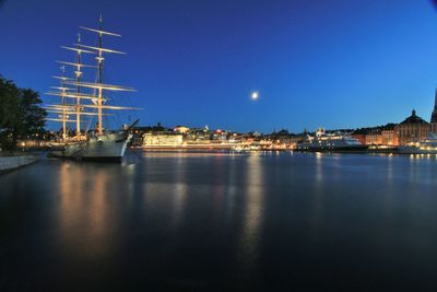 Boats moored at harbor against clear blue sky at night