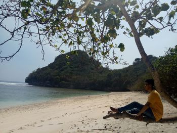 Woman sitting on beach by sea against sky