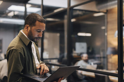 Dedicated businessman using laptop while standing in illuminated office