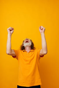 Rear view of woman with arms raised against yellow background