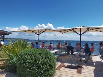 People relaxing on table by sea against sky